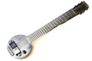 A frying pan guitar (also known as a fry pan guitar) lays flat with a white background. Rickenbacker Electro “Fry Pan” Lap Steel Guitar (c.1934)