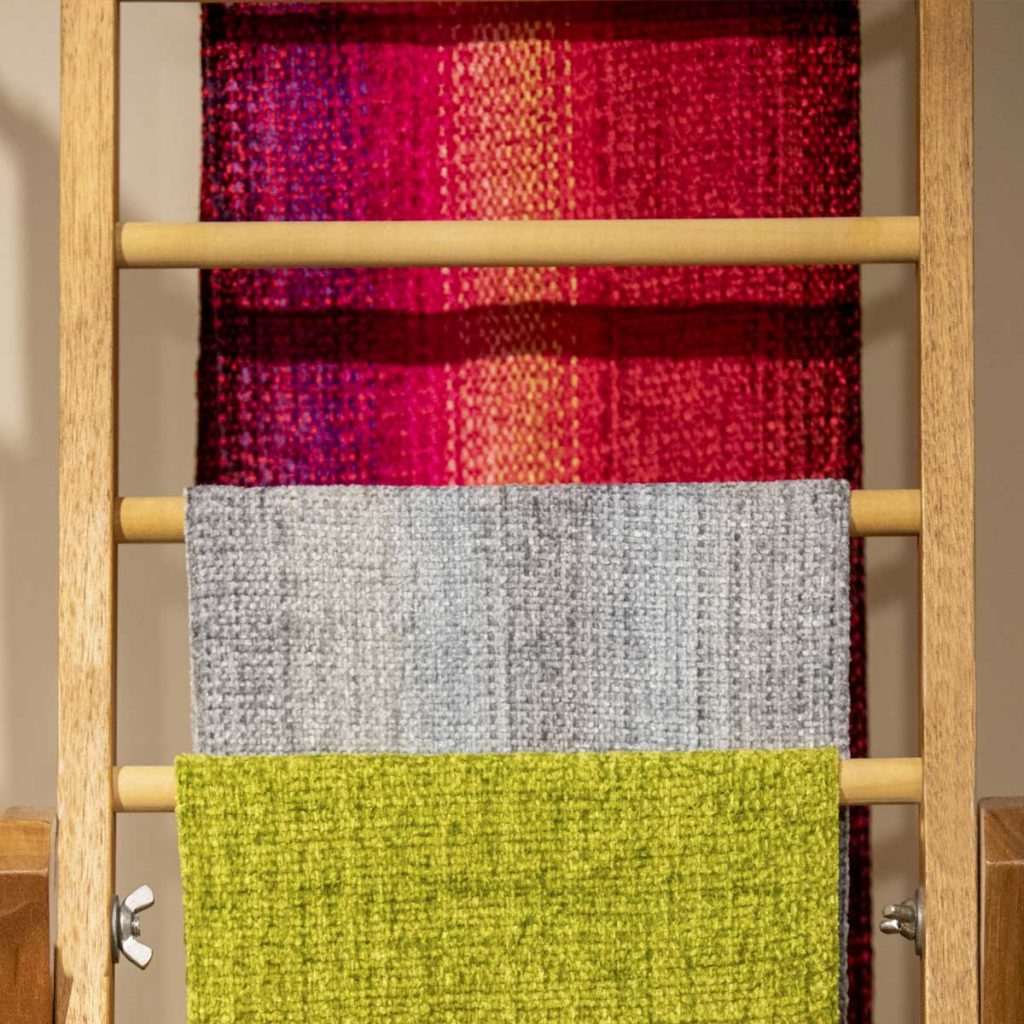 A wooden ladder-like pieces displaying several different colored scarves on the rungs.