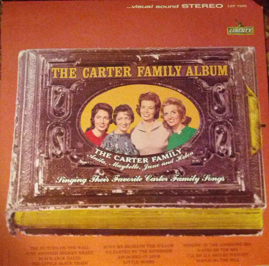 The Carter Family Album cover is a reddish-orange color with a leather bound, old photograph album shown in the center. The photograph album is labeled with the record's title "The Carter Family Album" and has an oval picture of Mother Maybelle, June, Anita, and Helen in the center.