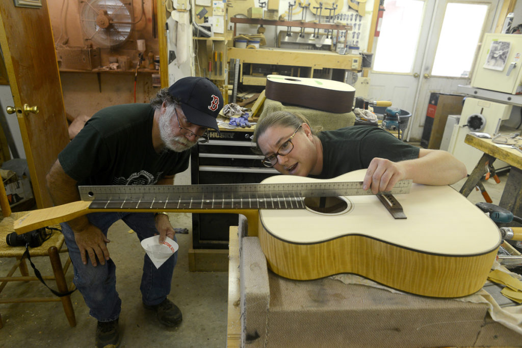 Wayne and Jayne Henderson measure the fretboard on a guitar-in-progress in Wayne's cluttered woodshop.